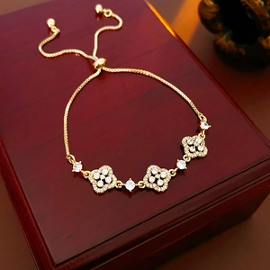 Detail of adjustable gold clover bracelet with white zircons on a luxury red wood jewelry box