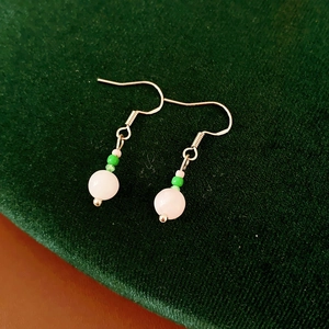 Detail view of pink crystal and green shell beads on silver hook earrings over green velvet