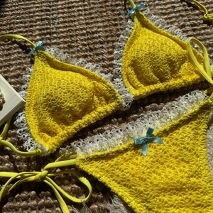 Detailed macro view of yellow crochet bikini with white lace trim and blue satin bows