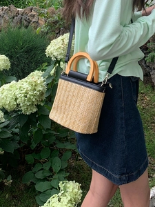 Detail of hand-woven straw bucket bag with wooden handle and black leather strap