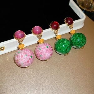Detail view of retro resin round pendant earrings in pink and green on a black jewelry box