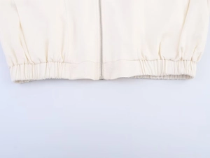 Detalle de chaqueta crema con cremallera de metal plateado y textura de dobladillo acanalado