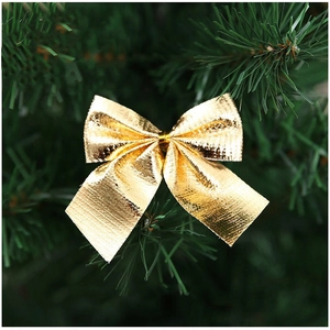 Golden Christmas bow ornament with metallic texture hanging on a green Xmas tree branch