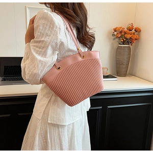 Detailed view of pink pleated tote bag with golden rings worn by a model in casual setting