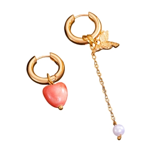 Detailed shot of asymmetrical gold earrings featuring a pink heart and hummingbird charm