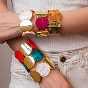 Dettaglio di ampi bracciali elastici in acrilico e metallo dorato multicolore