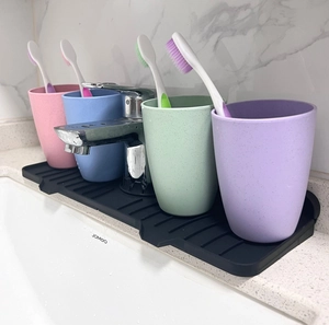 Macro shot of black silicone faucet mat for bathroom sink with colorful cups and toothbrushes
