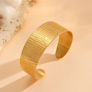 Detail of a wide gold cuff bracelet featuring embossed wood grain texture and metallic luster