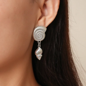 Close-up of a silver shell-shaped earring with metallic texture on a model's ear