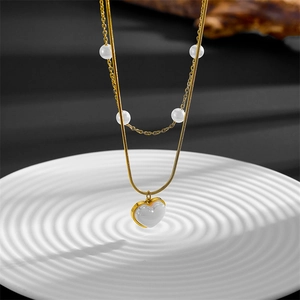 Detail of a double-layer gold snake chain with white pearls and a heart pendant