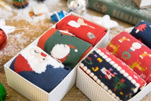 Christmas gift box with festive reindeer and snowman patterned socks on artificial snow
