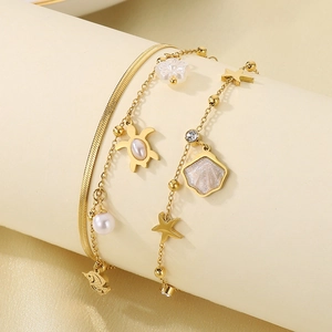 Detail of gold starfish and turtle charms on layered stainless steel anklet with pearls