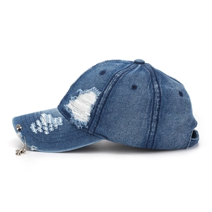 Detail of distressed denim baseball cap featuring metal safety pin and cross charm