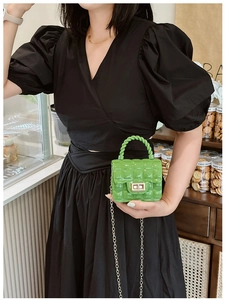 Detail of green quilted jelly bag featuring a gold twist lock and metal chain strap