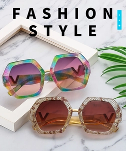 Detailed view of oversized hexagonal sunglasses with glitter frames and V-shaped metal logo