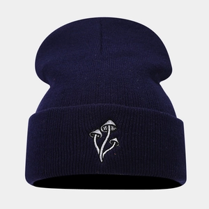 Dettaglio dei tre ricami a fungo bianco su un berretto in maglia blu scuro