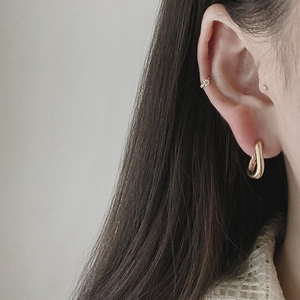Detail shot of a model wearing a gold U-shaped earring and a minimalist ear cuff set