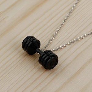 Close-up of a black dumbbell pendant and silver chain on a natural wood surface