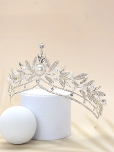 Detail of silver bridal crown with pearls and rhinestones on a white pedestal
