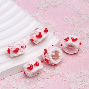 Detailed macro view of five pink and white resin cake-shaped beads with red hearts