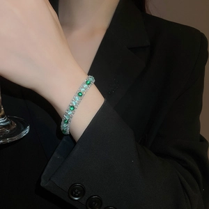 Close-up of dual-row bracelet with emerald green stones and cat-eye blue gems on wrist
