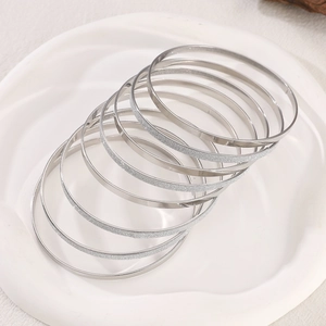 Detail of silver bangles with polished and frosted textures in a white ceramic dish