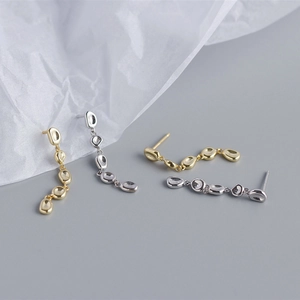 Macro view of metallic irregular pebble-shaped long tassel earrings in gold and silver