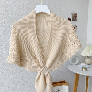 Detail of beige knit shawl with delicate hollow pattern and ribbon bow tie closure