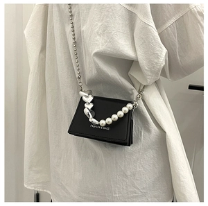 Detail of black crossbody bag with silver heart chain and white pearl handle detail