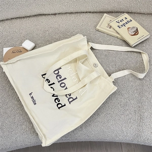Detail of cream canvas bag featuring beloved embroidery and metal magnetic closure