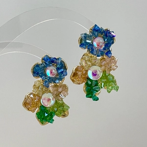 Détail de boucles d'oreilles fleur avec cristaux colorés bleus et verts sertis d'or chic