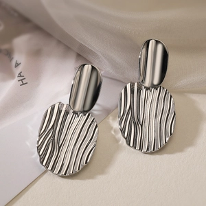 Minimalist silver geometric earrings with wavy texture on elegant white fabric background