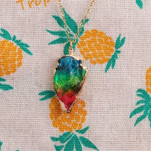 Close-up of rainbow crystal arrow pendant with gold trim on pineapple fabric