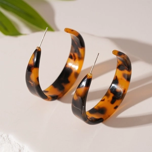 Gros plan sur des boucles d'oreilles en résine en forme de C avec imprimé léopard ambre