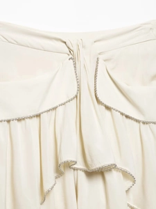 Detailed close-up of cream draped skirt fabric featuring elegant silver beaded trim edges