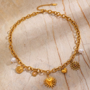 Dettaglio collana a maglia grossa oro con ciondoli a sole, cuore, scarabeo e perle