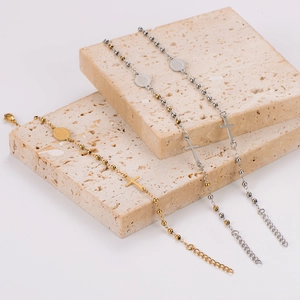 Minimalist stainless steel bead bracelet with cross pendant on beige stone display