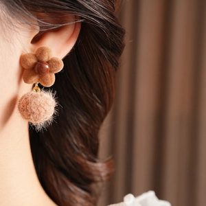 Detail of warm brown flocked flower and fuzzy pom-pom earrings on a model