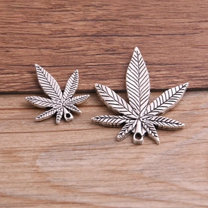Leaf shaped metal alloy pendants with intricate vein patterns on a wooden surface