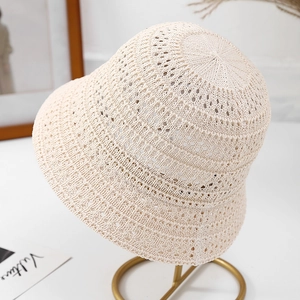 Detail of beige knit bucket hat with hollow pattern on a golden metal display stand