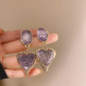 Dettaglio di orecchini vintage a cuore viola con eleganti cornici dorate e finitura strutturata
