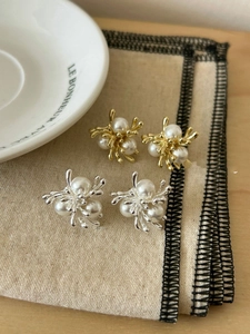 Macro detail of French vintage pearl stud earrings in gold and silver on beige fabric