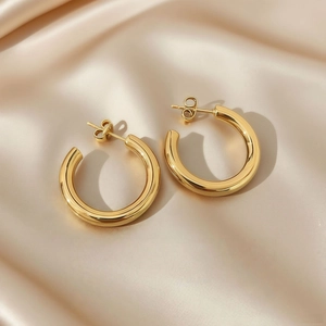 Detailed close-up of polished gold C-shape hoop earrings on a champagne silk background