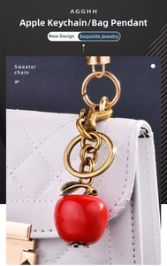 Macro detail of red apple keychain with gold lobster clasp on a white handbag