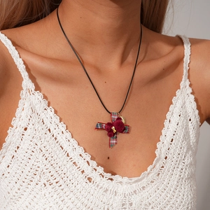 Plaid ribbon cross necklace with red faux fur pompom on black cord worn with white knitwear