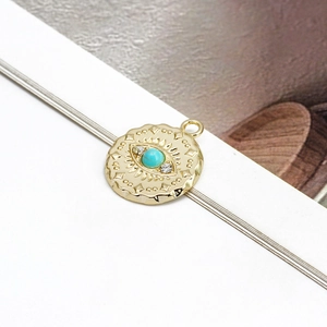 Detailed view of a gold evil eye pendant with turquoise bead and white rhinestones