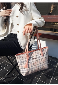 Detail of plaid tote bag with pink handles and metal logo held by model outdoors