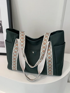 Dettaglio borsa tote verde scuro con tracolla a fantasia su un piedistallo bianco
