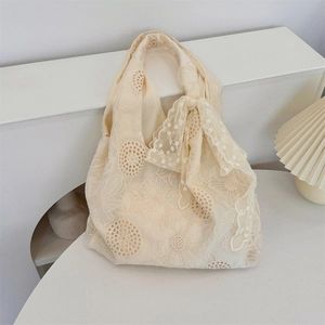 Close-up of floral embroidery lace detail and side bow on this cream white tote bag