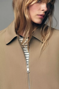 Détail d'une veste courte beige avec col à revers et fermeture éclair en métal argenté
